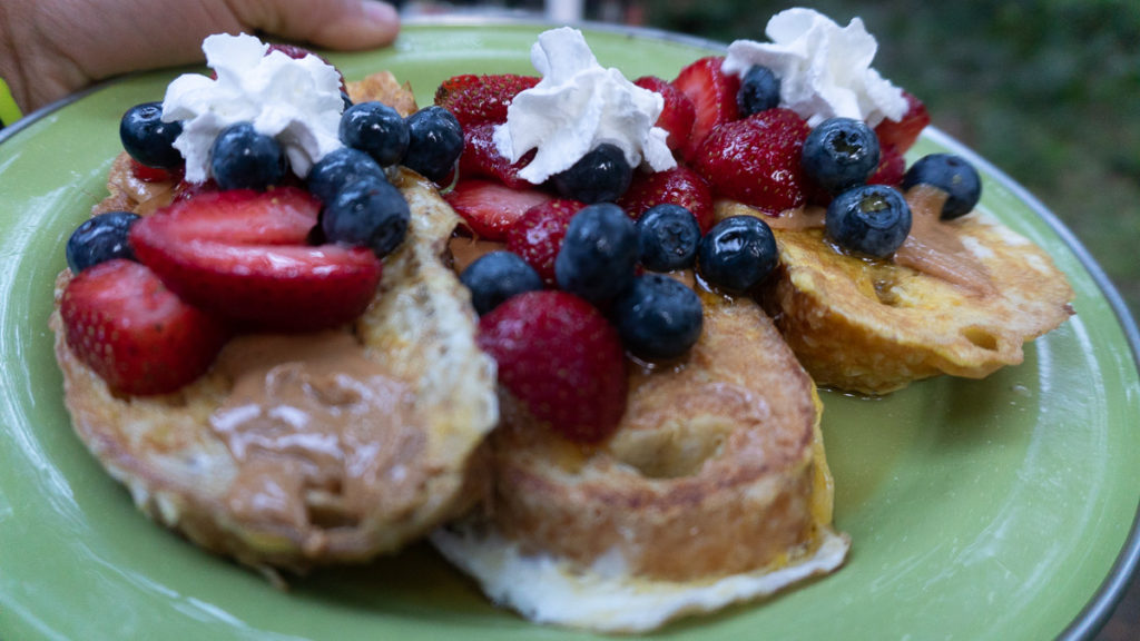 Thick french toast with fresh strawberries and blueberries, topped with whipped cream.
