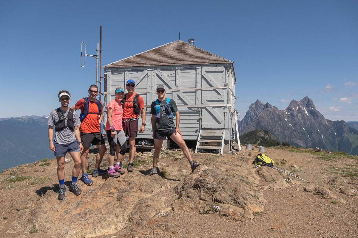 five trail runners stand in front of the Desolation Peak Fire Lookout in the North Cascades